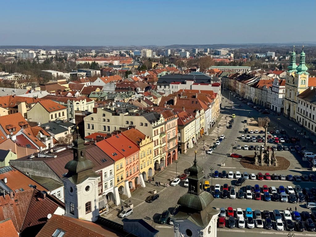 A view of a Czech city from above, with brightly colored buildings, orange roofs, a parking lot, and a few church towers sticking up.