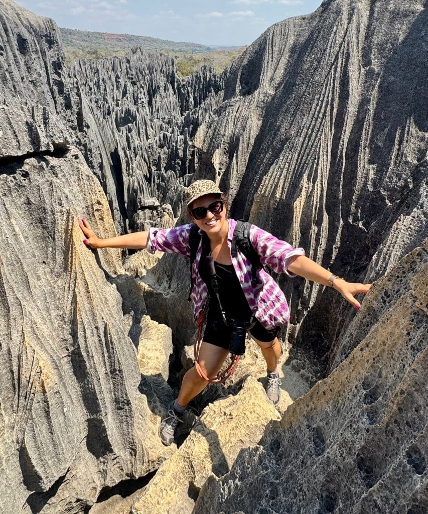 Kate standing between two spiky gray rock walls, holding on to both sides with a big grin on her face.