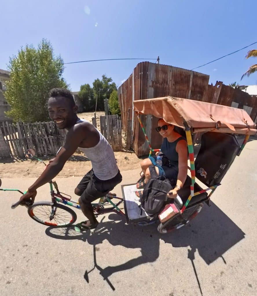 Kate riding in the back of a bicycle rickshaw. She and her driver grin at the camera.