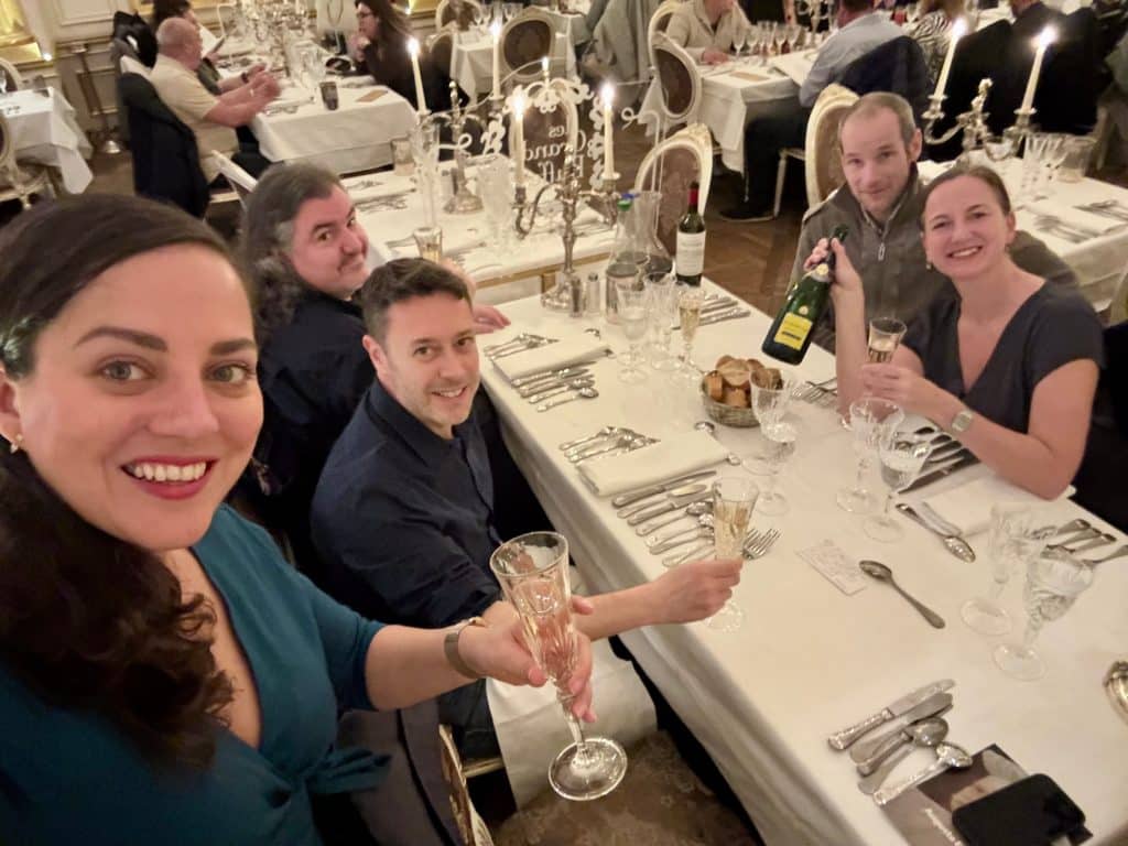 A selfie of Kate and her four friends around a dining table, holding up flutes of champagne and smiling.