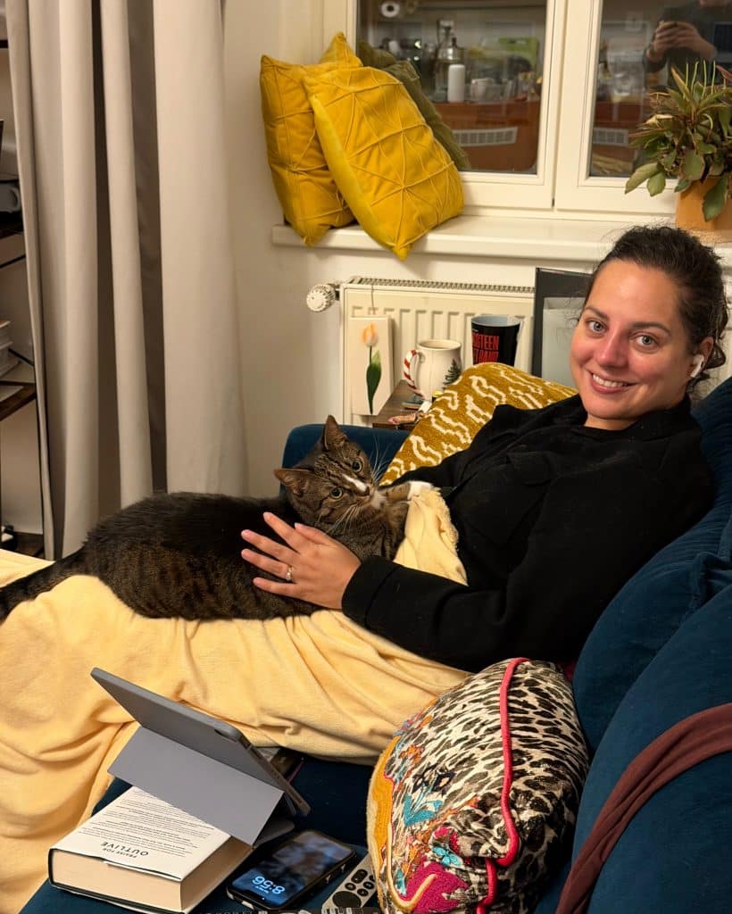 Kate holding Lewis the cat on her lap. He's sitting on a yellow blanket over her legs.