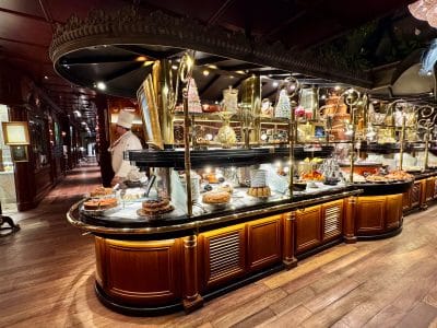 Several cakes and desserts sitting on a buffet table in a dark, wood-filled restaurant.