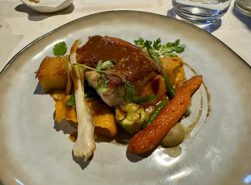 A plate with a filet of grilled fish and lots of vegetables, served over a vegetable puree.