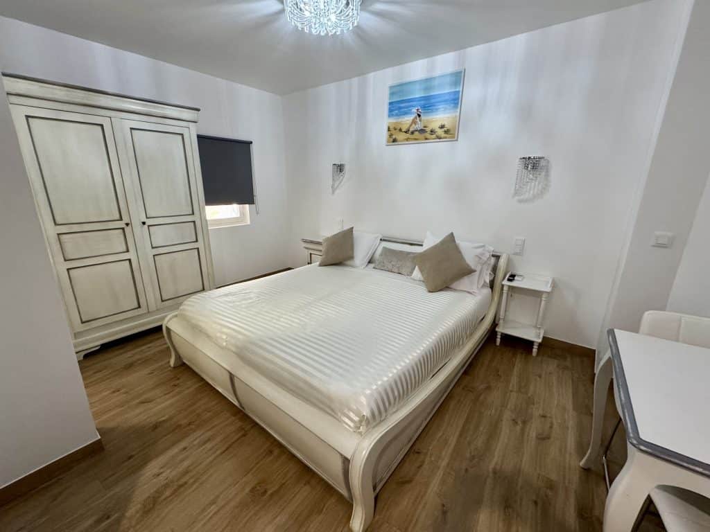 A hotel room with a queen-sized bed, a large white armoire, and a small dining table.