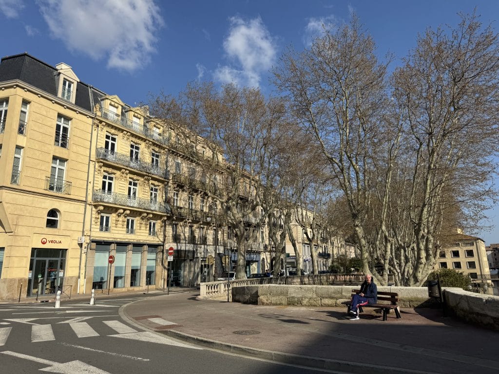 A yellow apartment building next to a few budding trees in Narbonne, France.