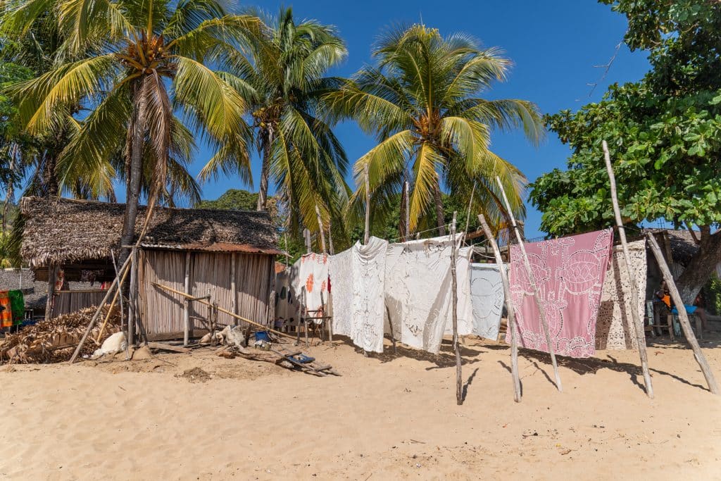 Beautiful woven sarongs hanging on a line, on a beach with lots of palm trees.