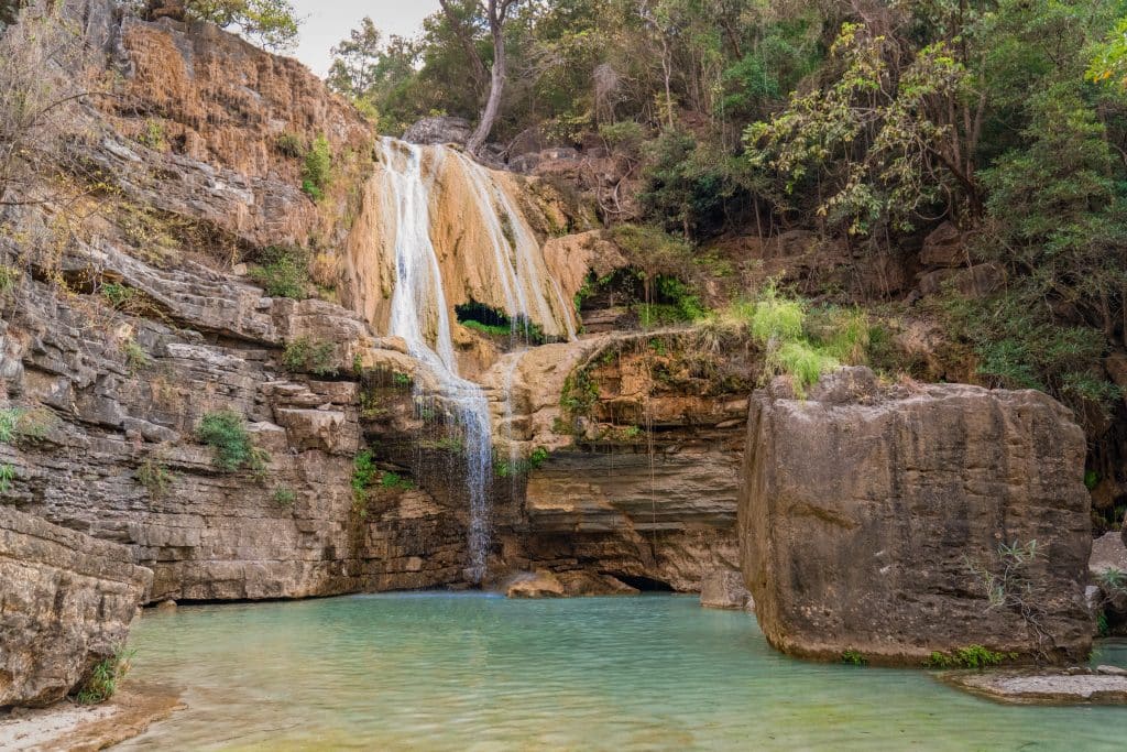 A small waterfall flowing over a rocky cliff into a bright turquoise pool below.
