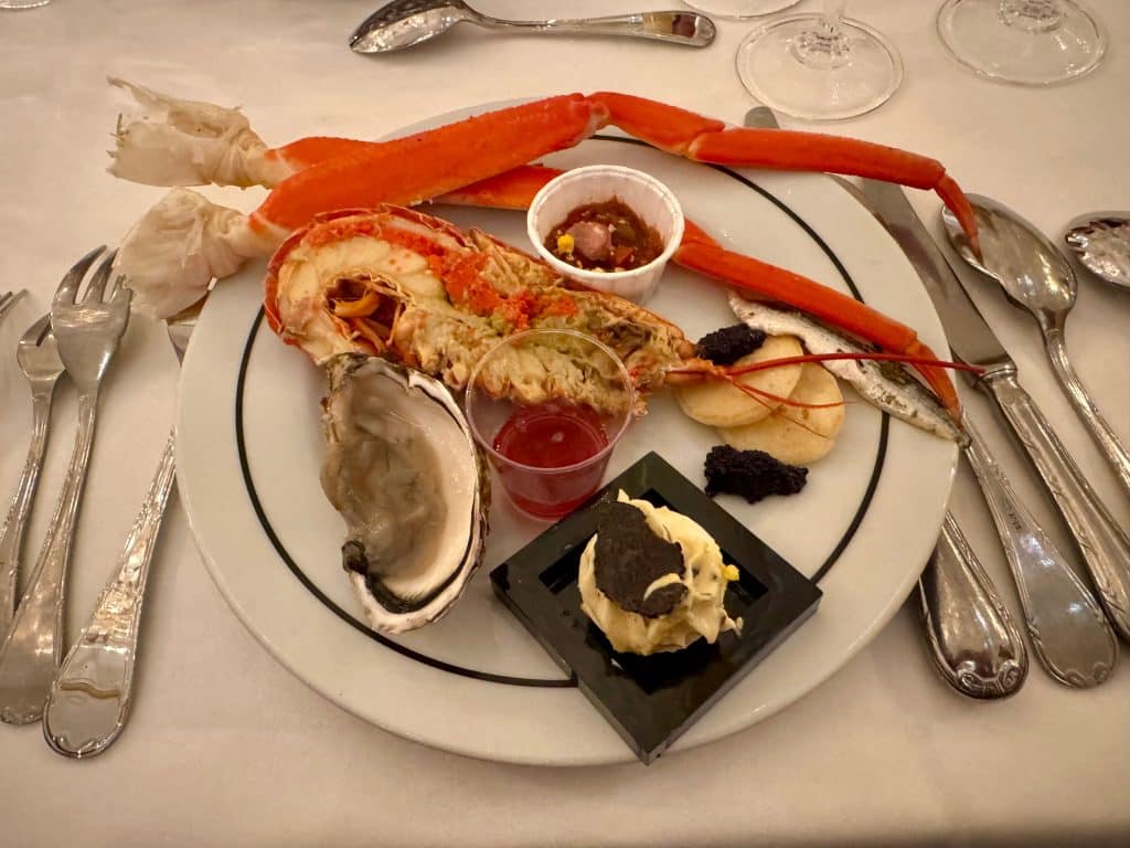 A plate of crab claws, an oyster, half a lobster, caviar on blinis, and an egg topped with black truffle.