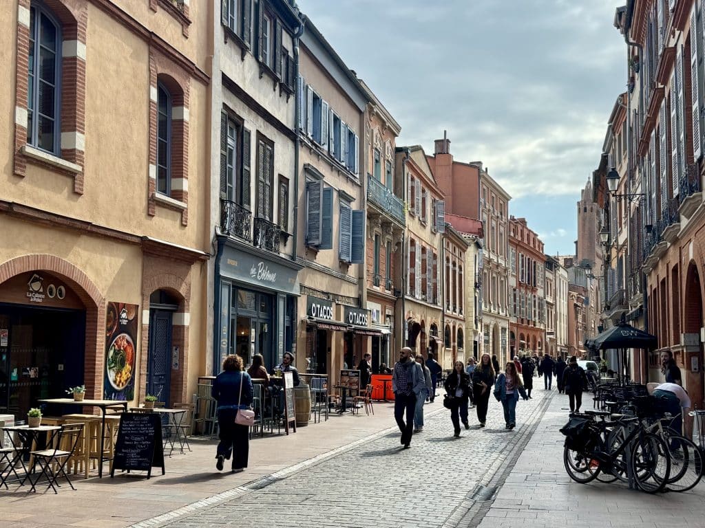 A street in Toulouse, France, with lots of buildings made of pinkish red brick and covered with pale blue shutters.