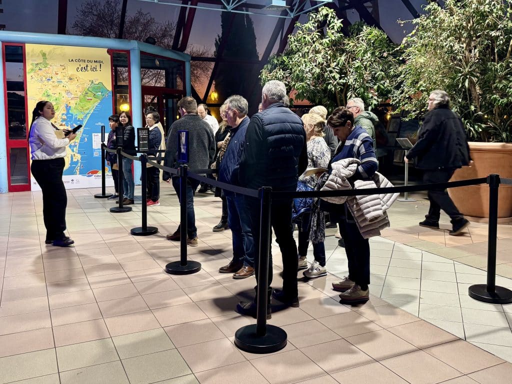 A group of people waiting in a partitioned line behind a velvet rope, as a worker looks over them.