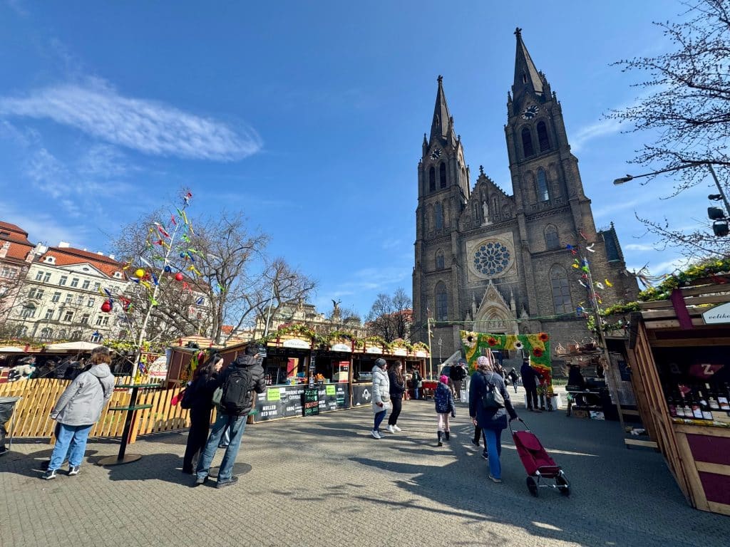 A square in Prague with a gothic church and several booths set up for Easter markets.