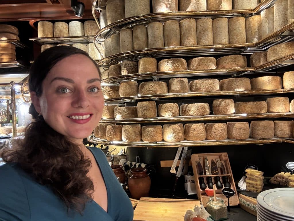 Kate takes a smiling selfie in front of shelves covered with different blocks of cheeses at the buffet.