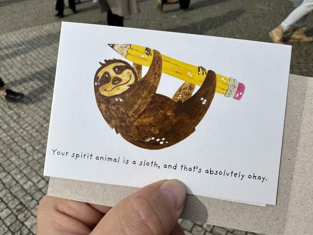 A card with a cartoon sloth holding a giant pencil. It reads "Your spirit animal is a sloth, and that's absolutely okay."