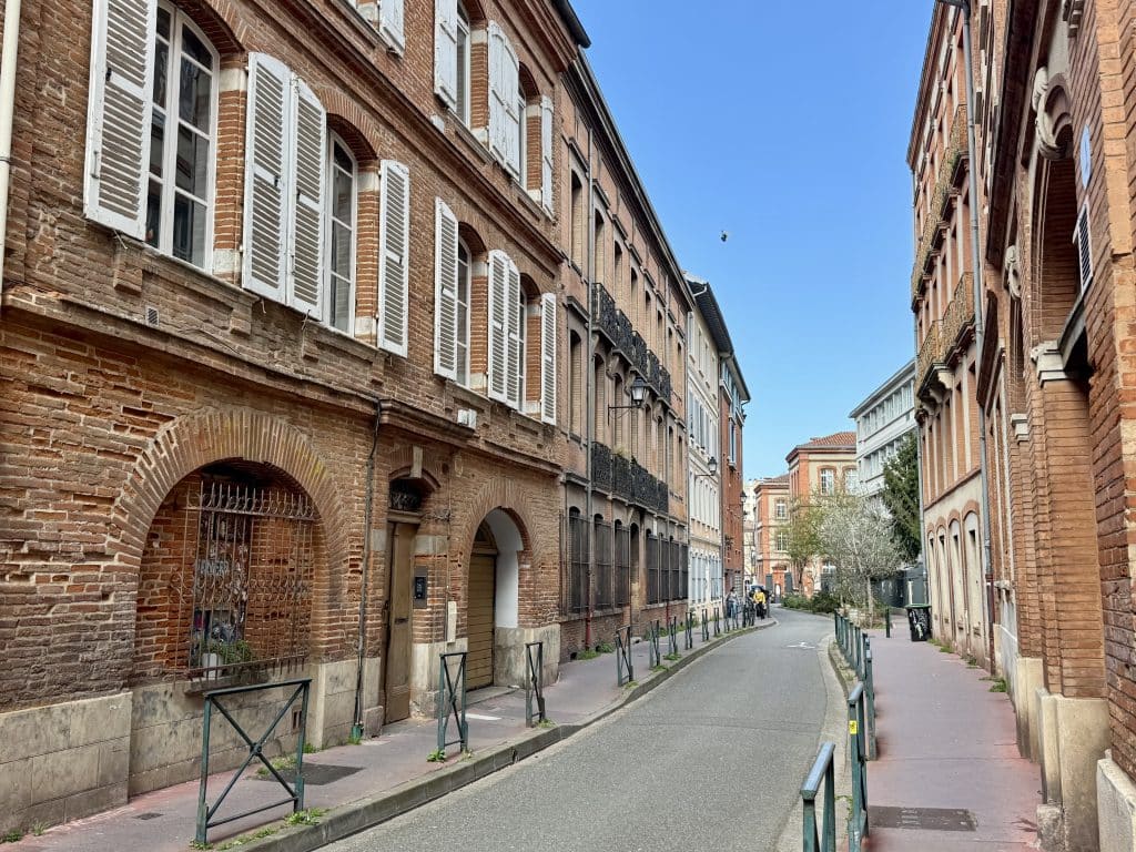 A street in Toulouse with pinkish red brick homes and white shutters.