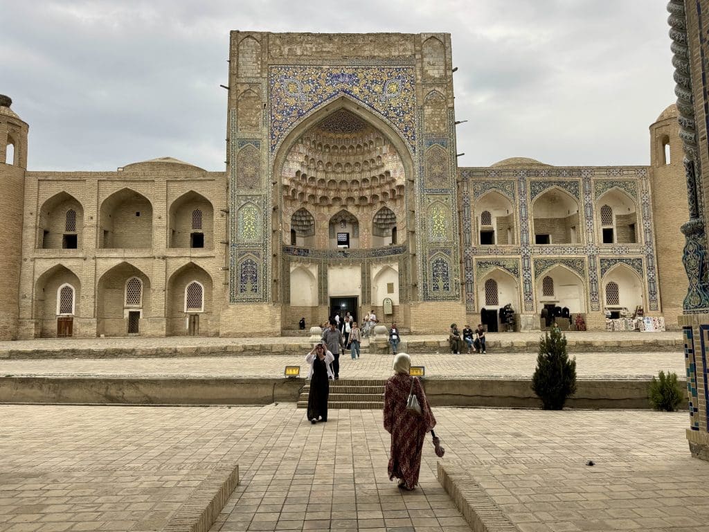 Women in headscarfs walking toward an old Uzbek school decorated with turquoise tiles.
