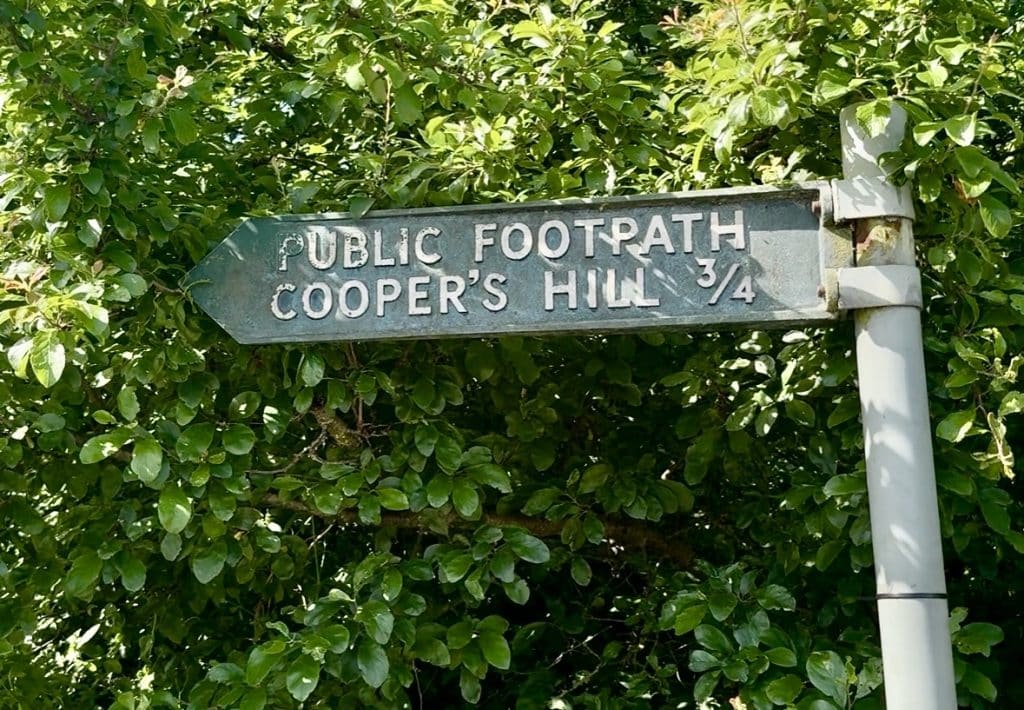 Sebuah tanda terselip di antara pepohonan bertuliskan Public Footpath Cooper's Hill 3/4.