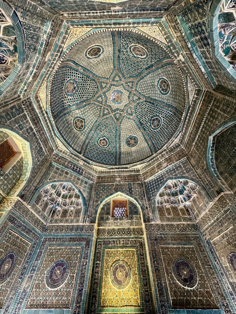 The inside of a mausoleum in Uzbekistan, covered with geometric patterns of blue, white, and turquoise tiles.