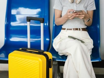 A woman sitting in a seat on her phone, a yellow suitcase next to her.