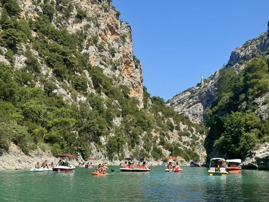 People boating on a bright green river between sides of a rocky gray and green canyon.