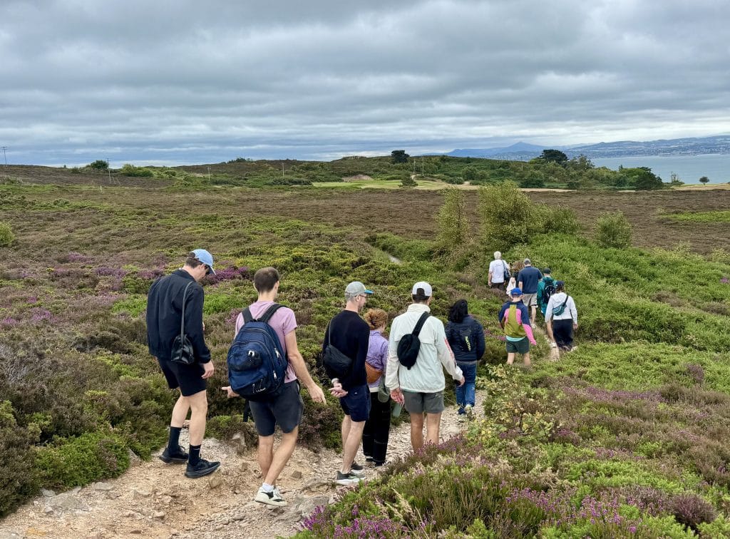 A group of friends hiking on a green hilltop in Ireland, underneath an overcast sky.