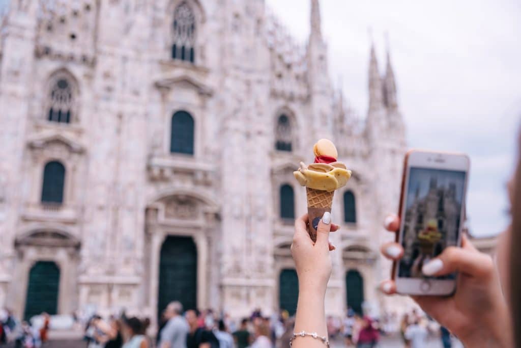 A hand photographing gelato in front of Milan's Duomo.