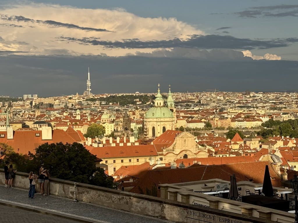 Prague's skyline at sunset, lit up in bright light but with dark blue clouds behind it.