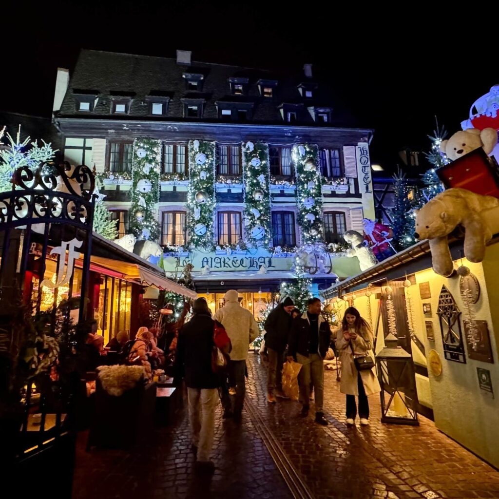 Beautiful half-timbered buildings in Colmar after dark, covered with twinkling Christmas lights and decorations.