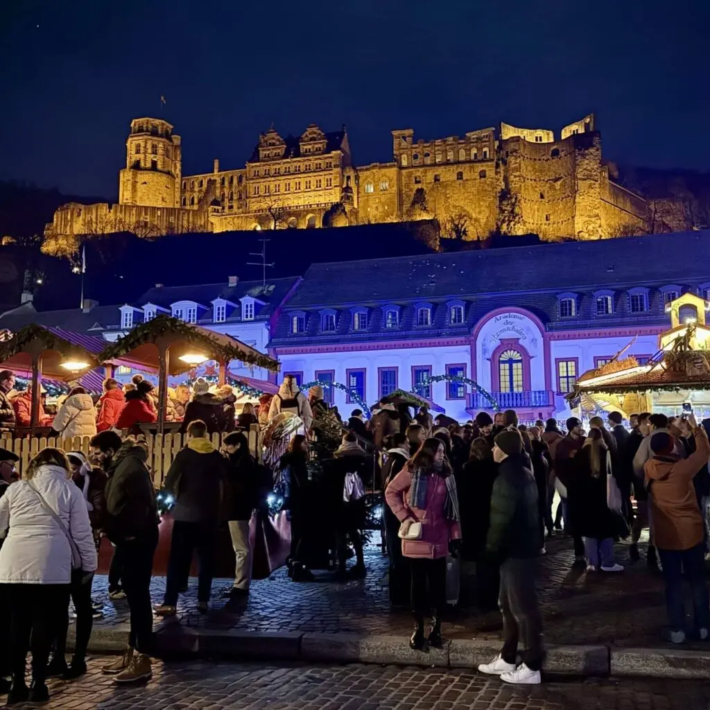 People gathering at a Christmas market in Heidelberg with a castle on the hill behind them