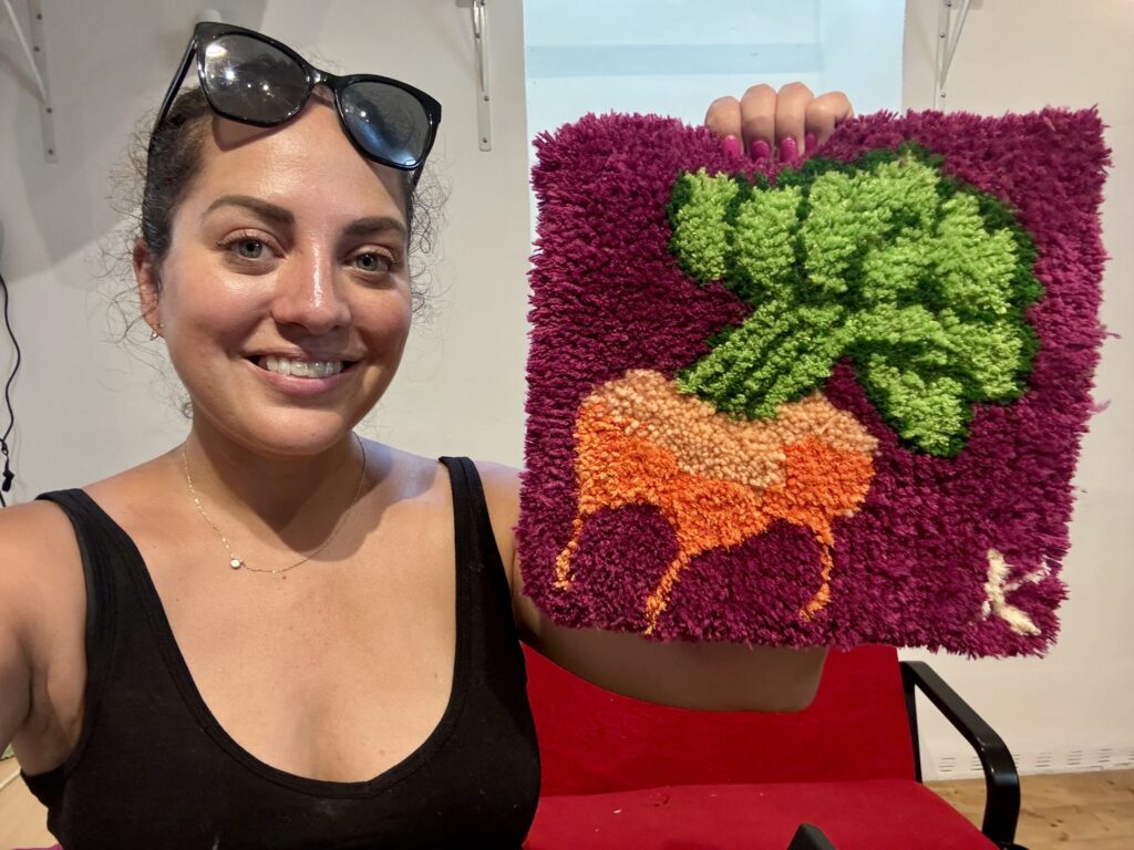 Kate holding up her small tufted rug, which has three golden beets on a purple background.
