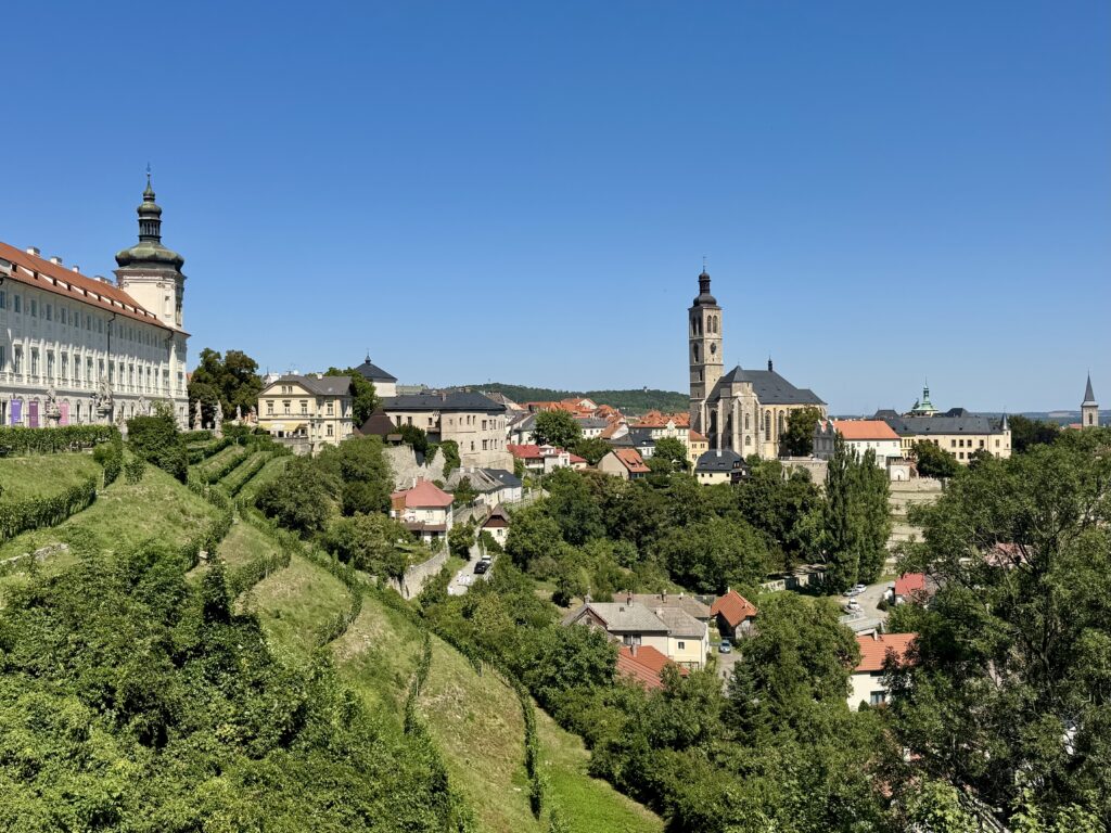 A panorama of the Czech town of Kutna Hora, with orange-roofed buildings, church towers, and white palaces above the hills.