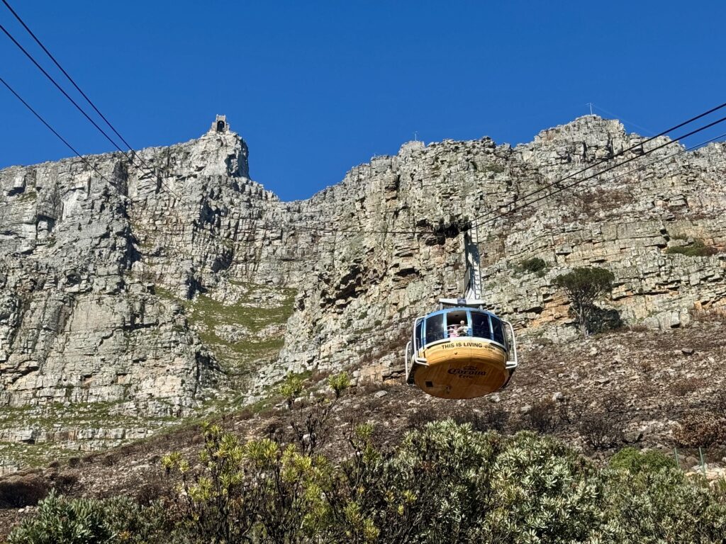 A yellow cable car coming down from the top of Table Mountain in Cape Town, underneath a bright blue sky.