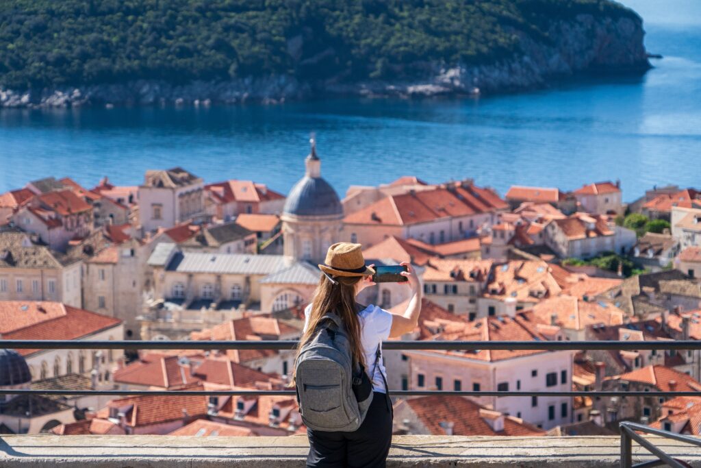 A woman taking a photo of Dubrovnik's orange-roofed skyline with her phone.